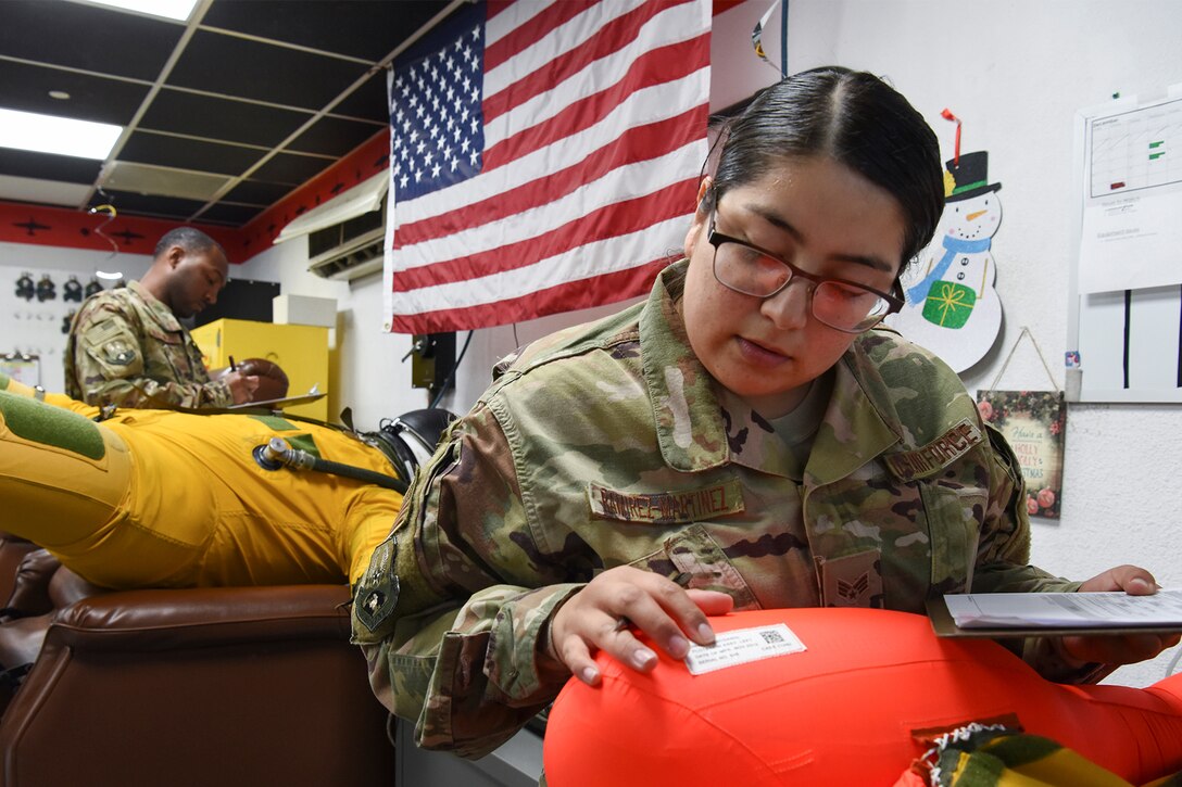 Service members inspect a pilot's full-pressure suit.