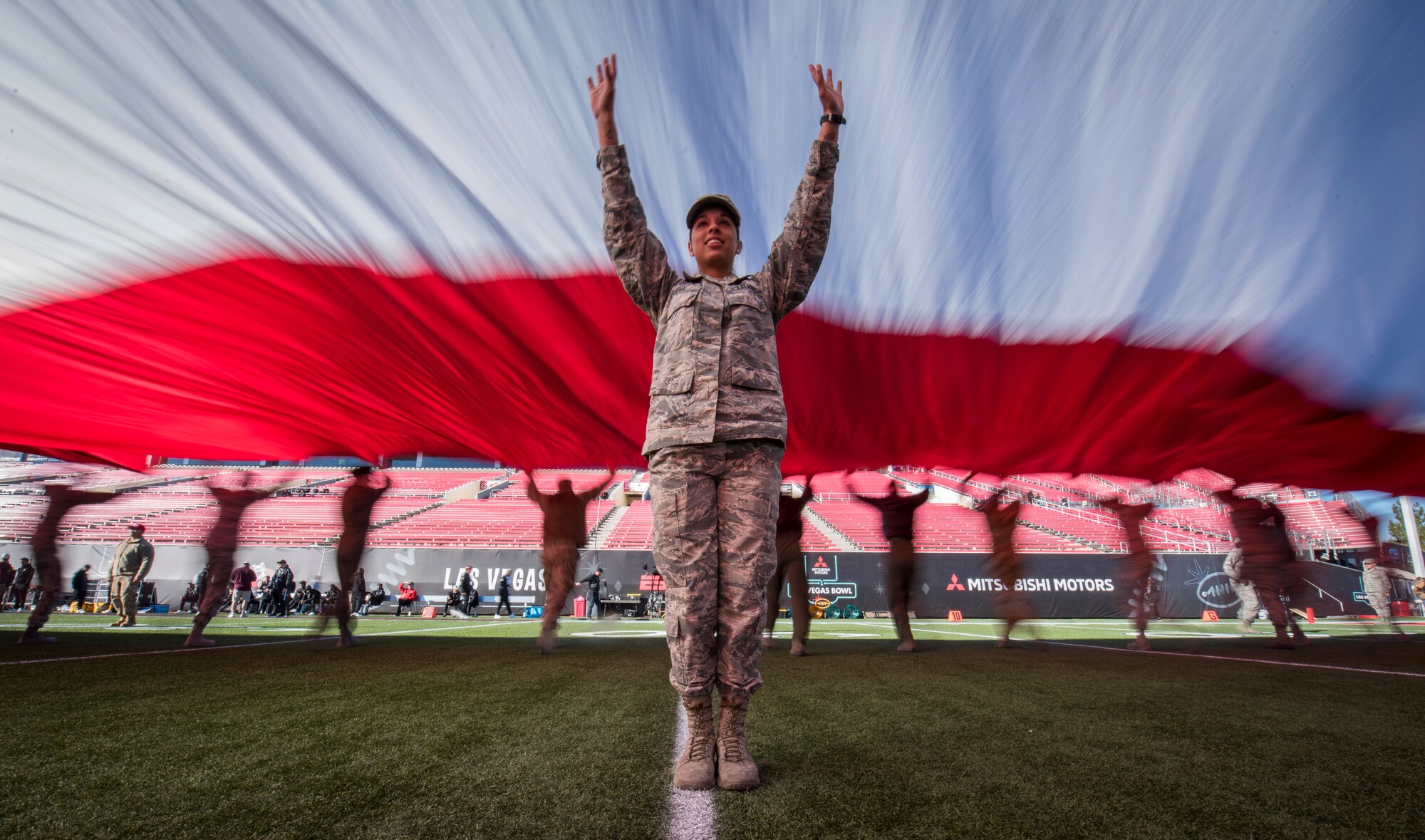 Airman 1st Class Ashley Libby, an aerospace medical technician assigned to the 99th Medical Operations Squadron at Nellis Air Force Base, Nevada, raises her arms to keep the American flag off the ground during the 2018 Las Vegas Bowl opening ceremony at Sam Boyd Stadium in Las Vegas, Dec. 15, 2018. The half-ton flag required more than 200 Airmen to carry it. (U.S. Air Force photo by Senior Airman Andrew D. Sarver)