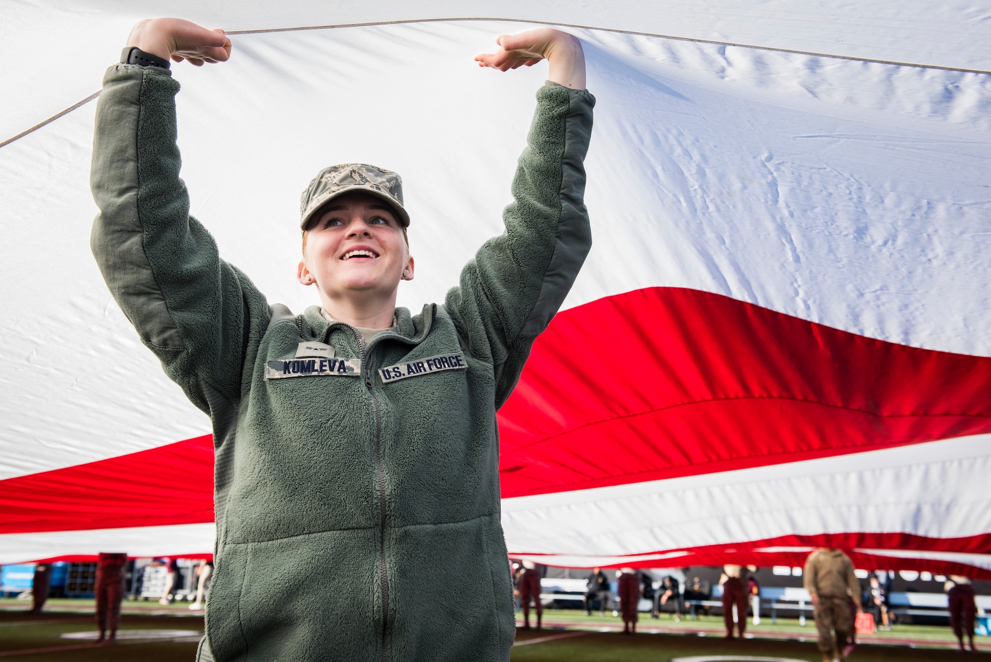 Airman 1st Class Lolita Komleva, a pharmacy technician assigned to the 99th Medical Operations Squadron at Nellis Air Force Base, Nevada, lifts her arms to help keep a half-ton American flag off the ground during the 2018 Las Vegas Bowl opening ceremony at Sam Boyd Stadium in Las Vegas, Dec. 15, 2018. Komleva was one of more than 200 Airmen who volunteered to carry the giant flag. (U.S. Air Force photo by Senior Airman Andrew D. Sarver)