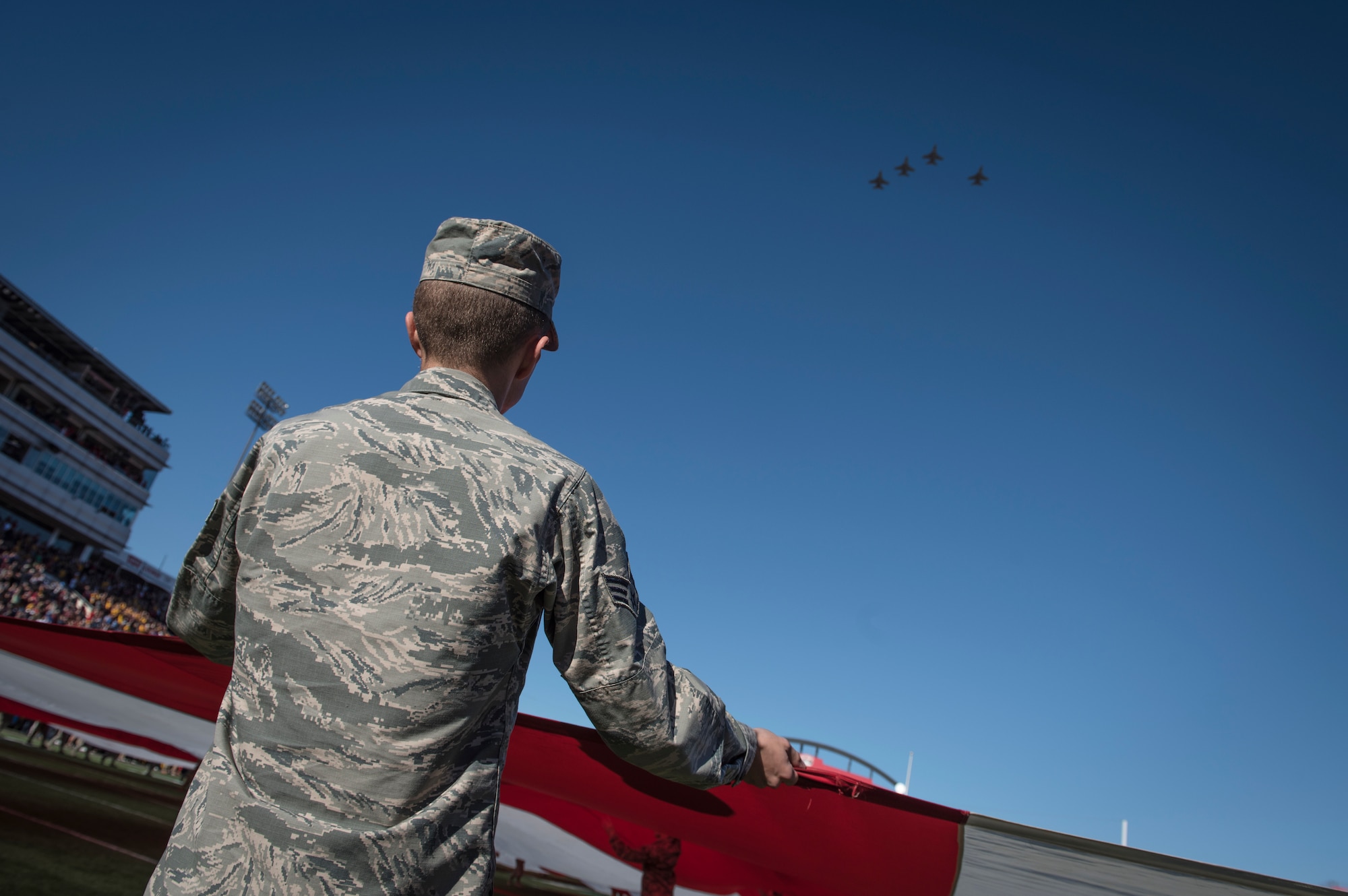 Senior Airman Garrett Tarpley, a fuels distribution specialist assigned to the 99th Logistics Readiness Squadron at Nellis Air Force Base, Nevada, carries part of a half-ton American flag, while four F-16 Fighting Falcon fighter jets assigned to the 24th Tactical Air Support Squadron at Nellis fly overhead during the 2018 Las Vegas Bowl opening ceremony at Sam Boyd Stadium in Las Vegas, Dec. 15, 2018. The 2018 Las Vegas Bowl featured the Arizona State University Sun Devils versus the Fresno State University Bulldogs. The Bulldogs won 31-20. (U.S. Air Force photo by Senior Airman Andrew D. Sarver)