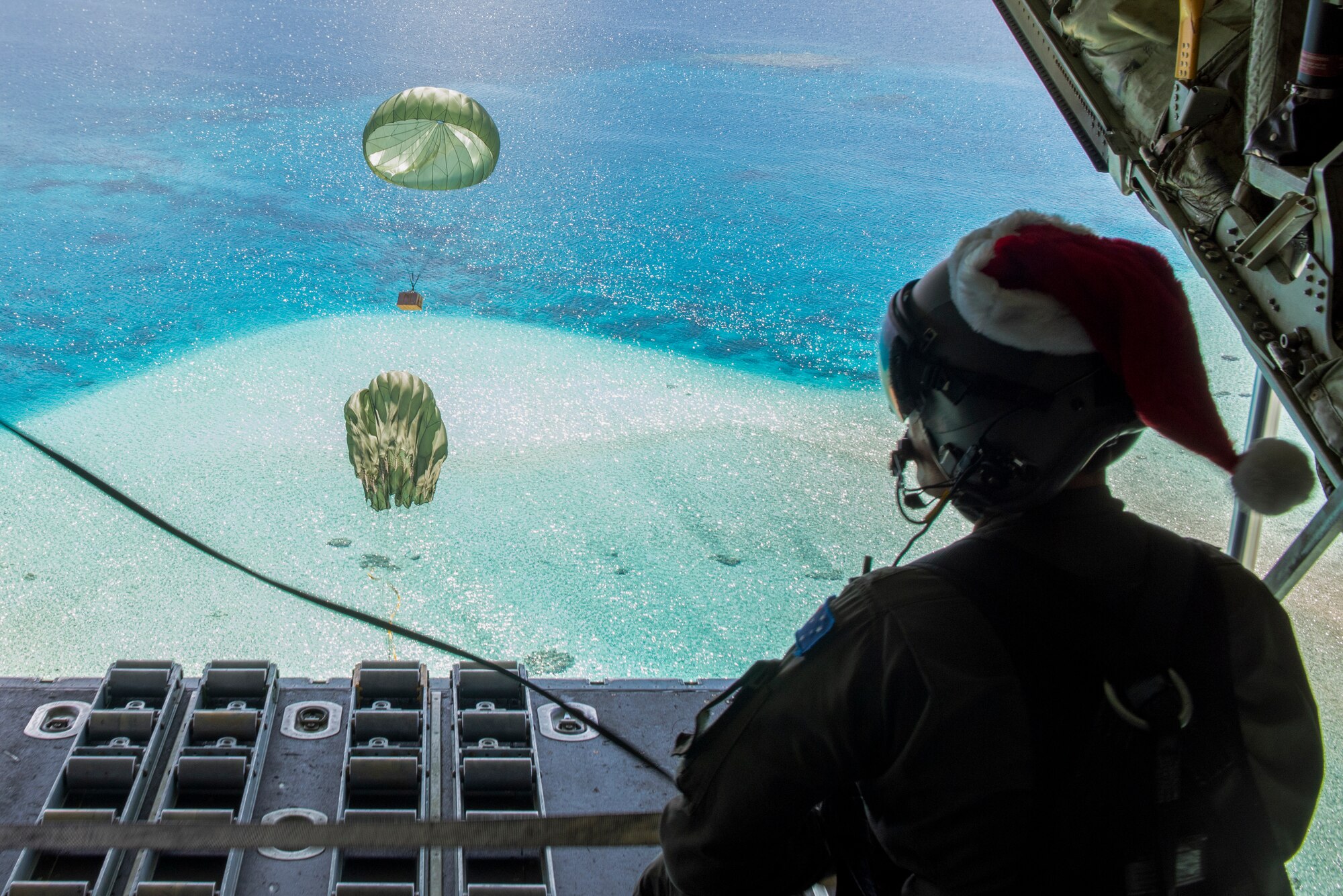 Royal Australian Air Force SGT Karl Penny, 37th Squadron C-130J Super Hercules loadmaster out of RAAF Base Richmond, Australia, looks out as the parachute for a Low-Cost, Low-Altitude bundle carries humanitarian aid down to the atoll of Kapingamarangi, Federated States of Micronesia (FSM), during Operation Christmas Drop 2018, Dec. 13, 2018. Every December U.S. Air Force crews from Yokota Air Base, Japan team up with the Japan Air Self-Defense Force (Koku Jietai) and RAAF to airdrop supplies to the Commonwealth of the Northern Marianas, FSM, and the Republic of Palau. (U.S. Air Force photo by Senior Airman Matthew Gilmore)