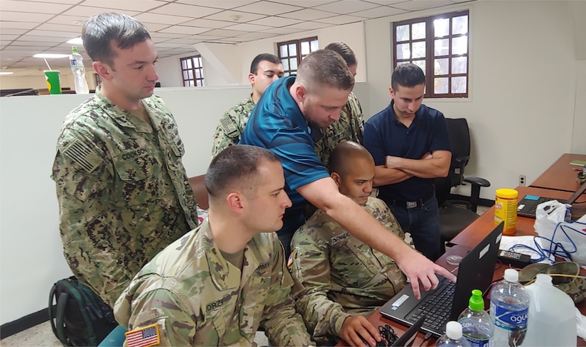 Ben Loader, Department of Homeland Security (DHS) personnel, middle, and Lt. Marcus Guevara, right, observe Staff Sgt. Asiel Conde, 600 Cyber Protection Team, center, setting up network tools at Soto Cano Air Base, Dec. 2018.