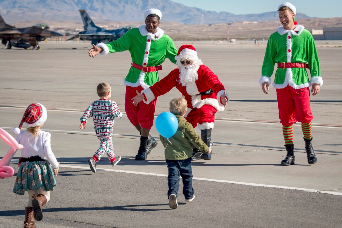 Kids run on a flightline toward Santa and two elves waiting to greet them.