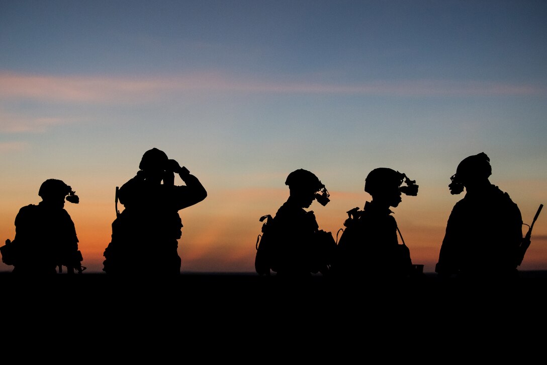 The figures of five soldiers are silhouetted against the darkening sky.