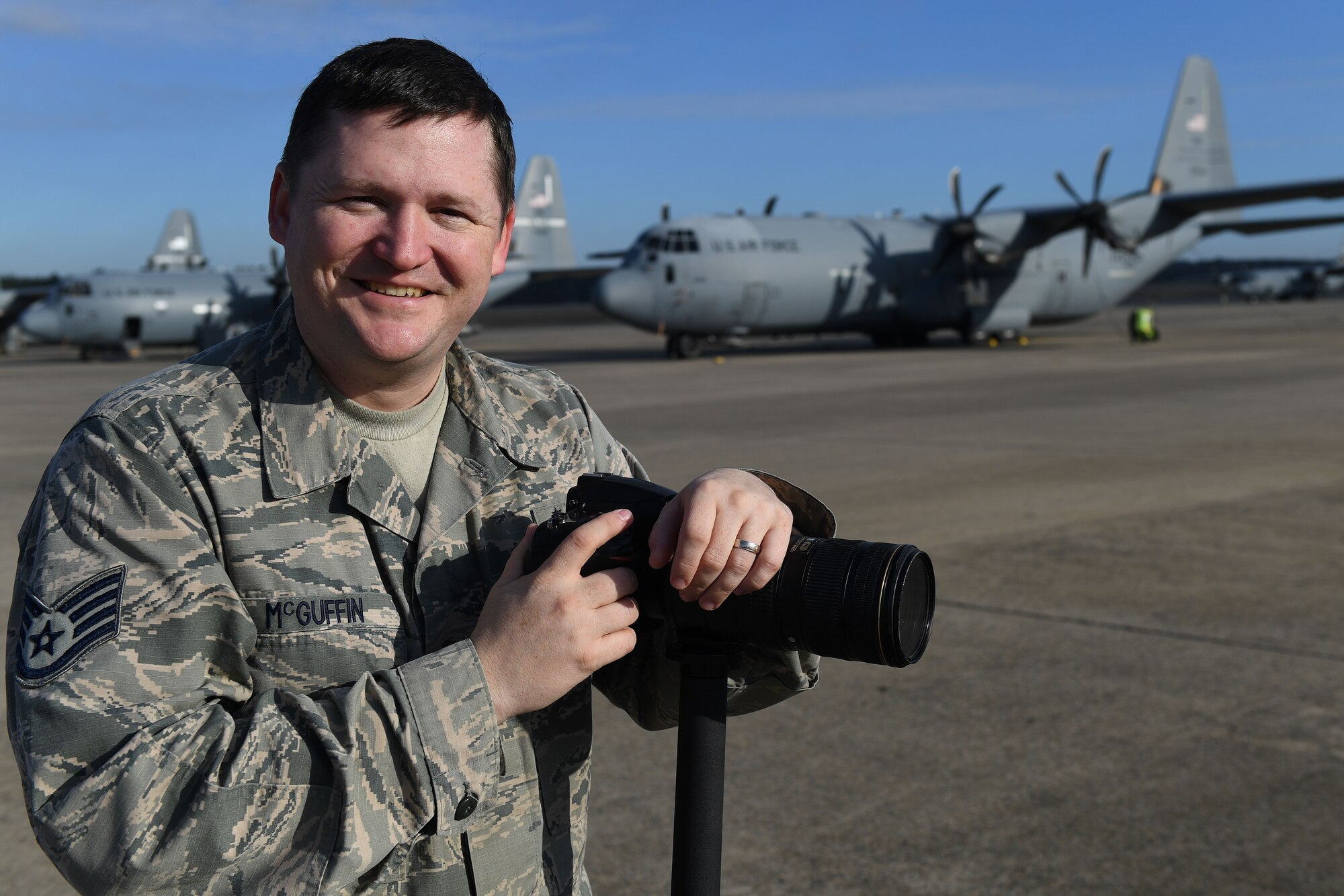 A man poses with a camera in front of a C-130.