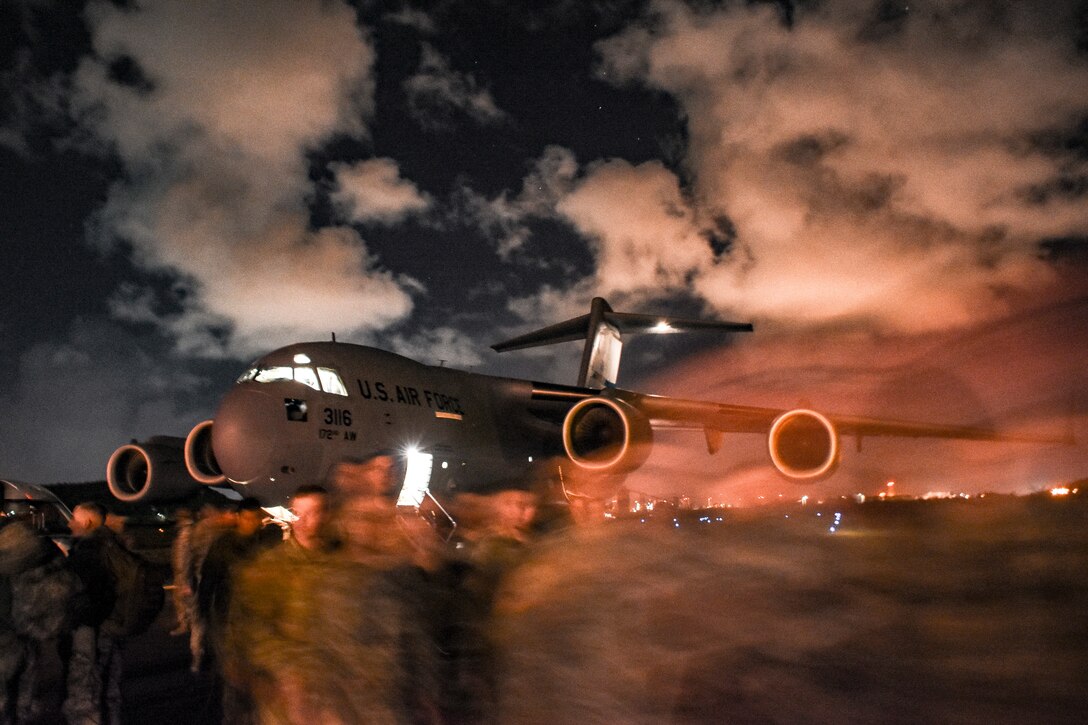 National Guard soldiers walk  away from a C-17 in the early morning.