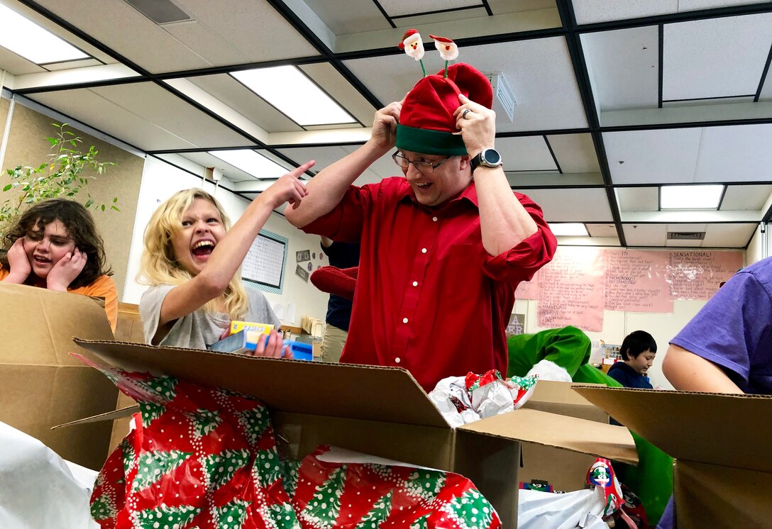 Master Sgt. Michael Johnson, 67th Aerial Port Squadron, helps Shayla unpack a box of gifts during a Christmas party at Mound Fort Junior High in Ogden