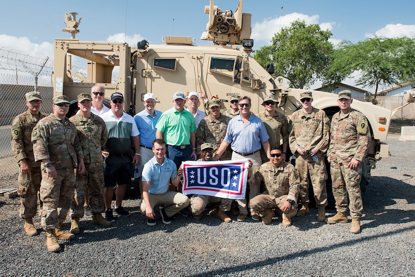 Golfers pose with troops and a USO flag by an Army tank.