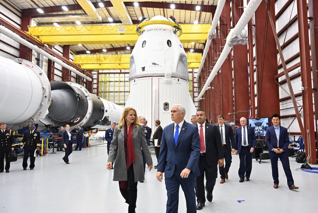 Vice President Mike Pence walks with group of people in front of a space capsule.