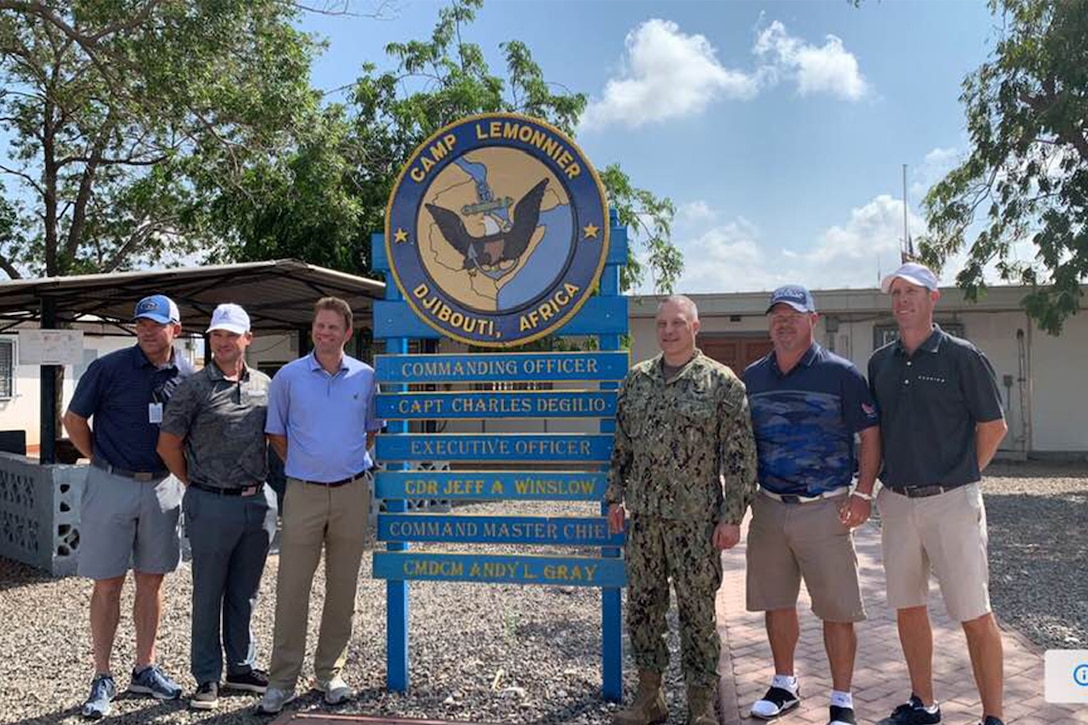 Golfers stand with Camp Lemonnier’s commanding officer in front of a building.