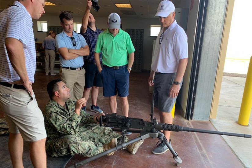 A sailor shows golfers how to use a massive gun.