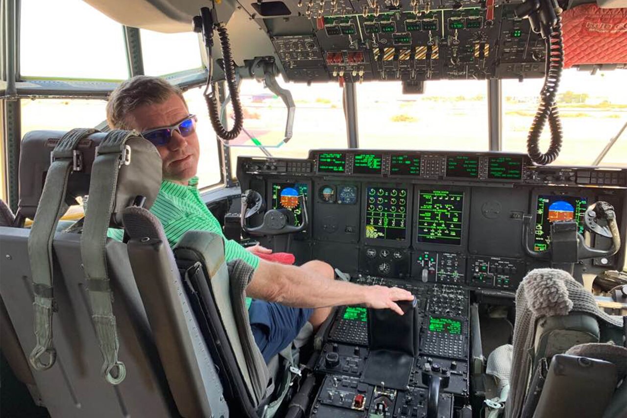 A golfer sits in the pilot’s seat of a C-130 cockpit.