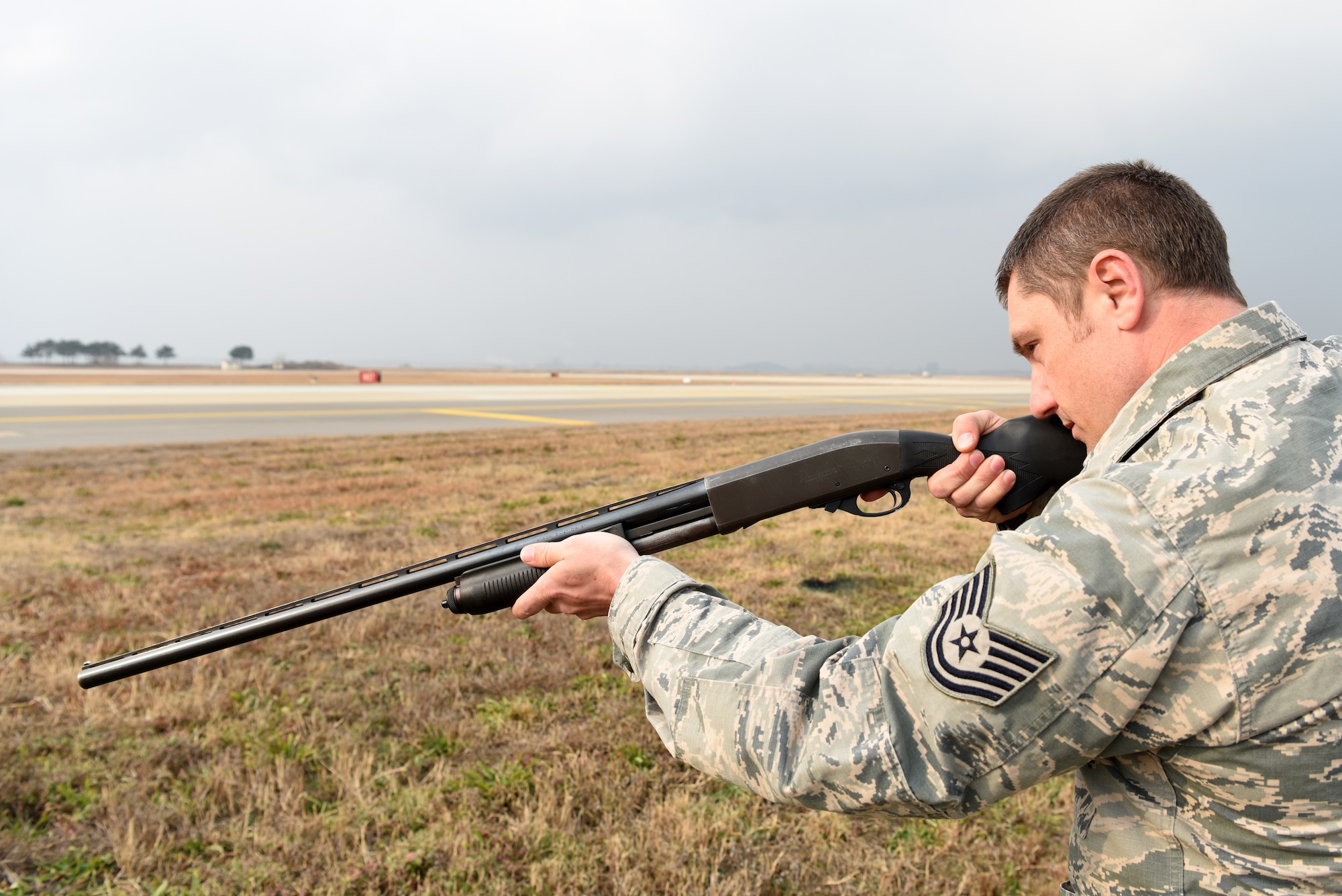 U.S. Air Force Tech. Sgt. Erick Hall, 8th Operations Support Squadron aircrew flight equipment lead trainer, aims a shotgun near the runway at Kunsan Air Base, Republic of Korea, Dec. 13, 2018. Hall is among more than 40 volunteers at Kunsan who ensure the runway is clear of birds and other wildlife during takeoffs. (U.S. Air Force photo by Staff Sgt. Joshua Edwards)