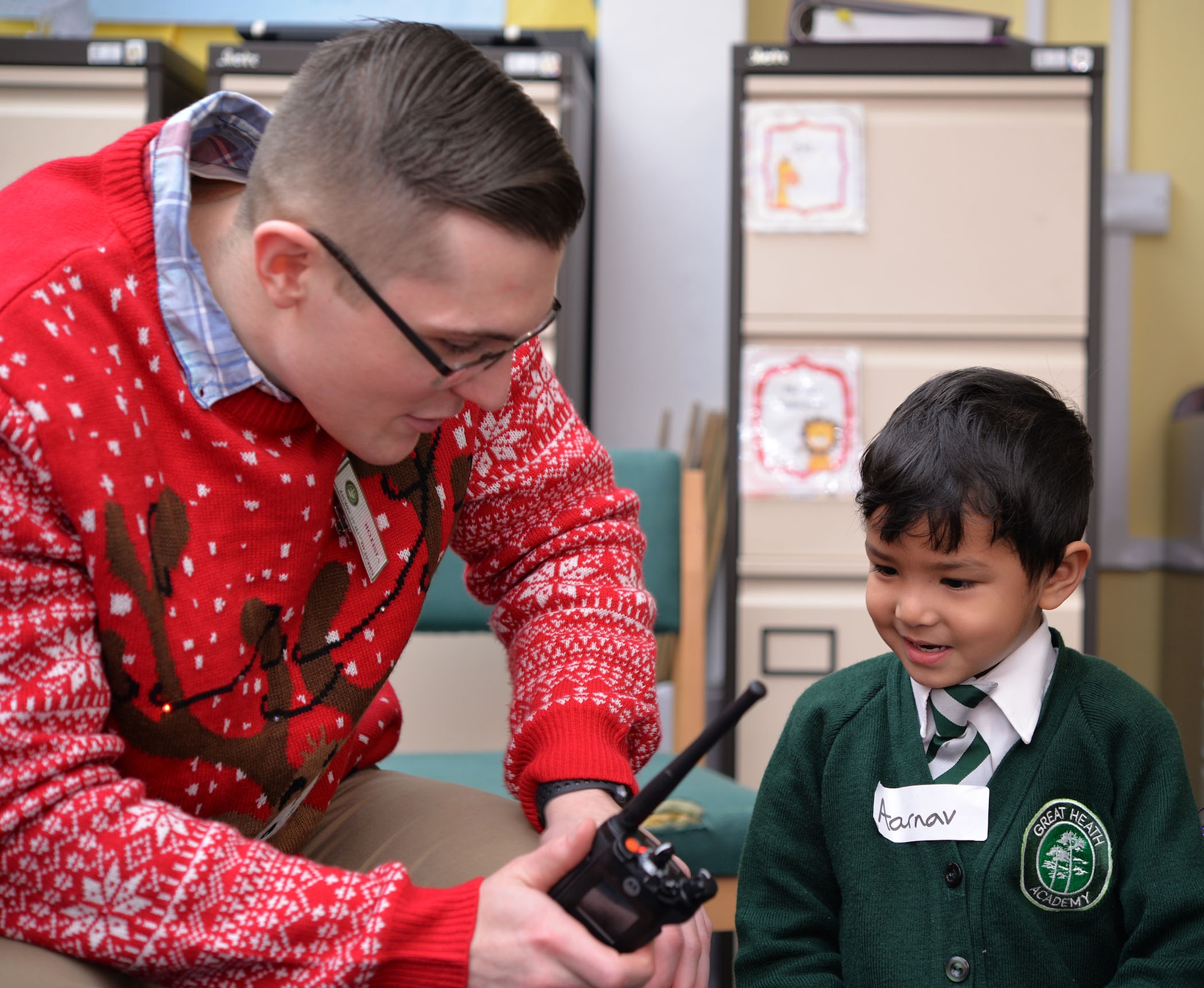 U.S. Air Force Senior Airman Roy Smith, 100th Communications Squadron radio frequency transmissions systems technician, operates a radio as an early years student from Great Heath Academy, Mildenhall, Suffolk, talk with Santa Dec. 18, 2018. A team of three Airmen from RAF Mildenhall visited Great Heath Academy and Beck Row Primary Academy to give students a chance to talk to Santa about what presents they would like for Christmas. (U.S. Air Force photo by Karen Abeyasekere)