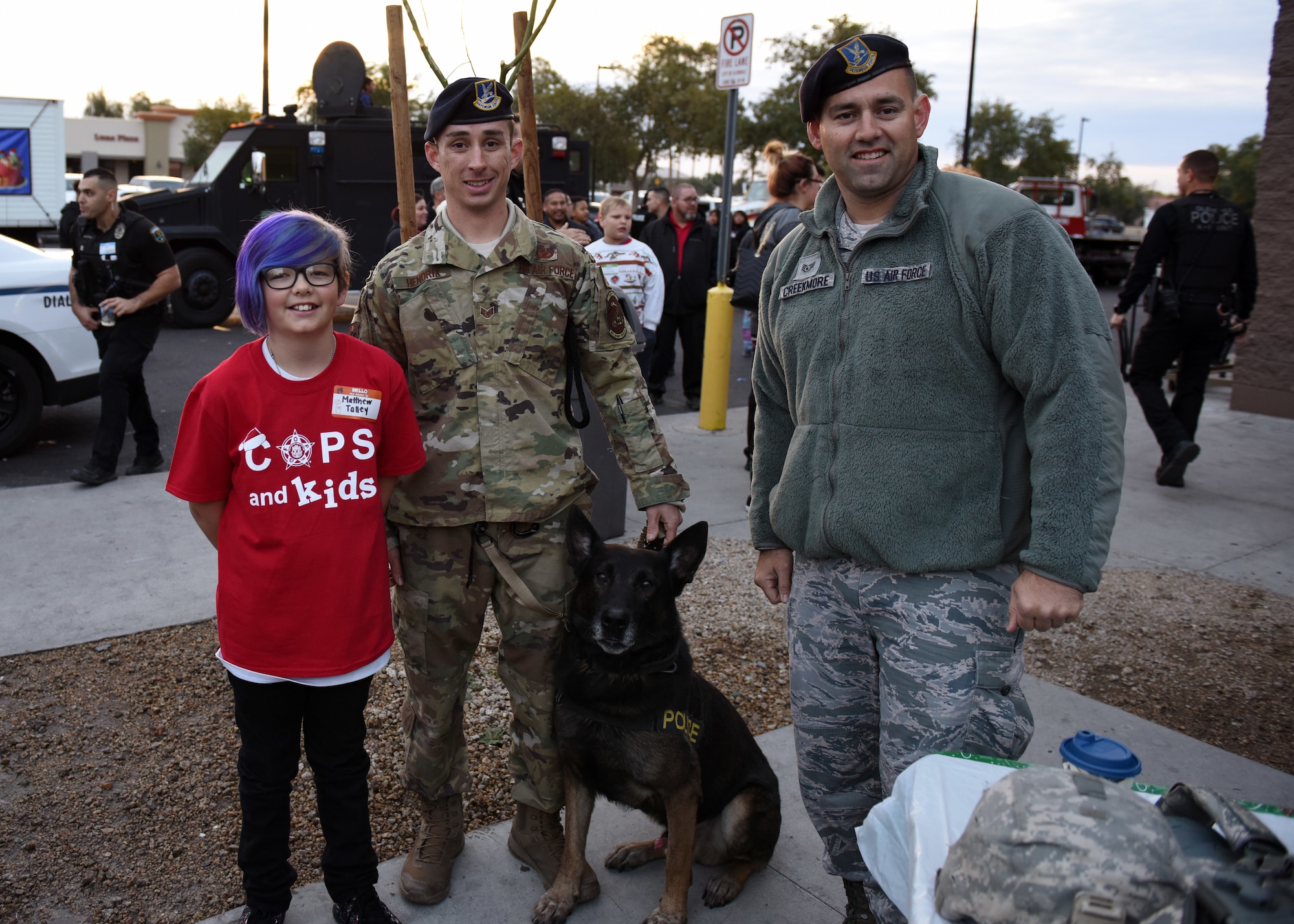 Staff Sgt. Tyler Hendrix, 56th Security Force Squadron military working dog trainer, and Staff Sgt. Eric Creekmore, 56th SFS investigator, pose with a child during the annual Glendale Shop with a Cop charity event in Glendale, Ariz., Dec. 15, 2018.