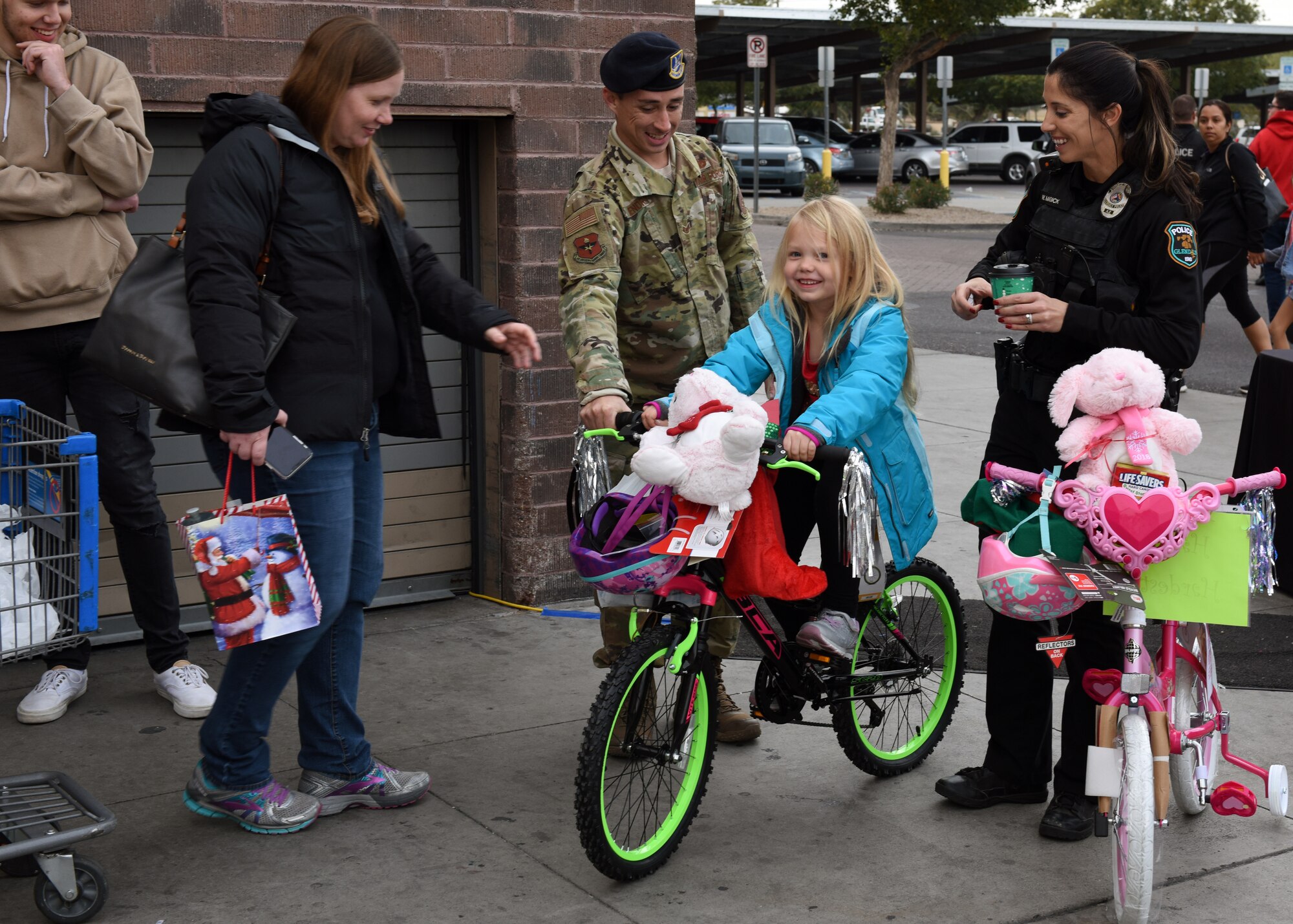 Staff Sgt. Tyler Hendrix, 56th Security Force Squadron military working dog trainer, guides a bike that a child received at the Glendale Shop with a Cop event, in Glendale, Ariz., Dec. 15, 2018.