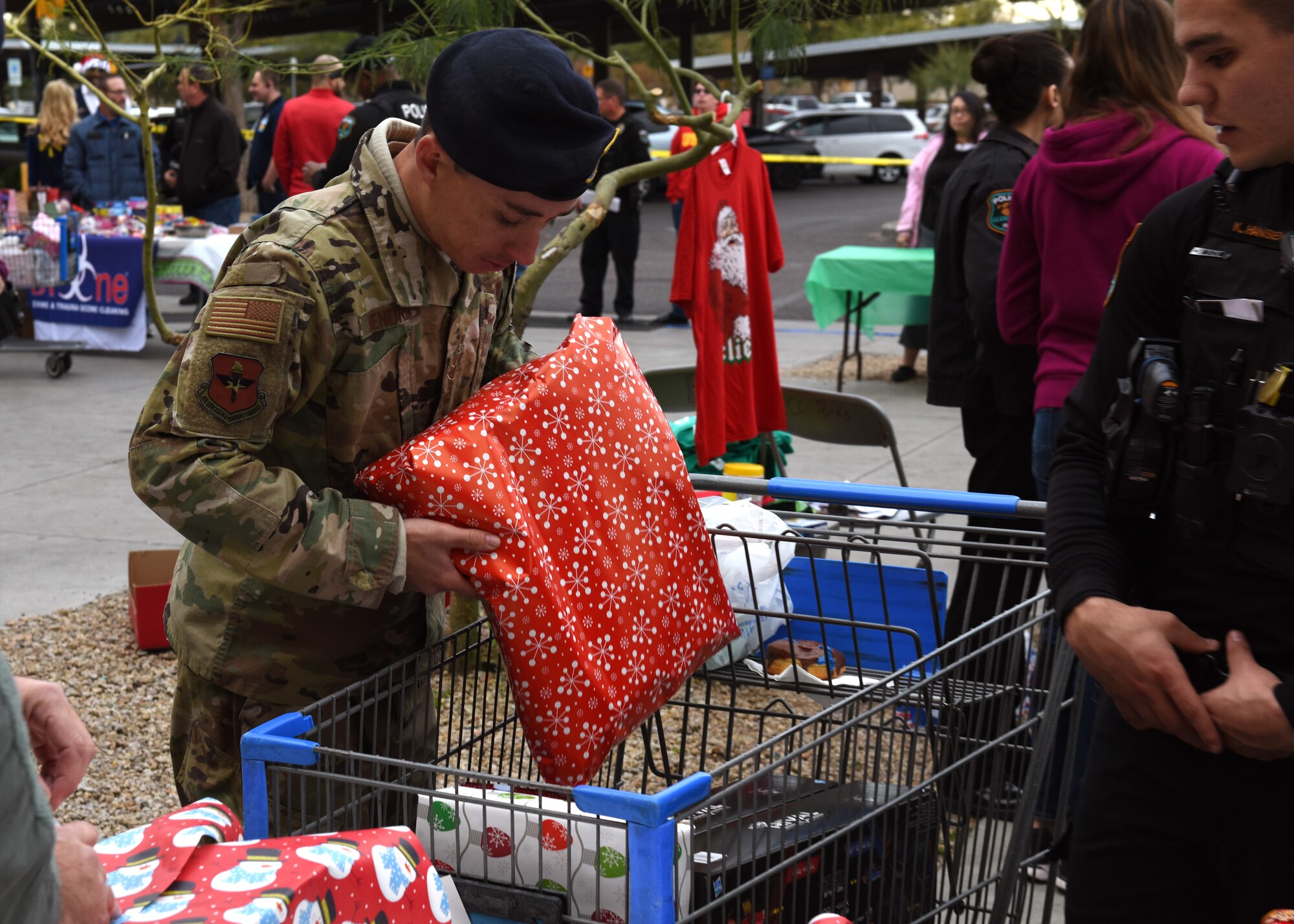 Staff Sgt. Tyler Hendrix, a Security Force Squadron military working dog trainer, places a present inside a cart at the Glendale Shop with a Cop event, in Glendale, Ariz., Dec. 15, 2018.