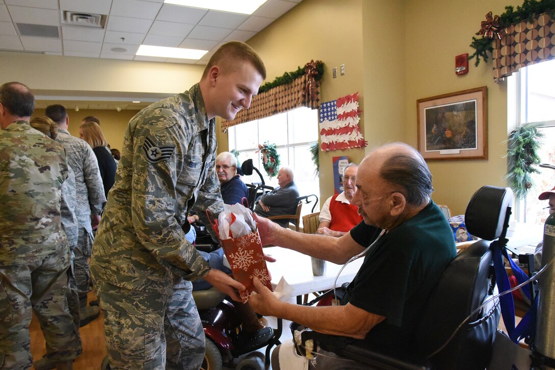 U.S. Air Force Staff Sgt. Nathan Reitan, of the 119th Wing, delivers a Christmas gift to Army Veteran Marvin Hieb at the North Dakota Veterans Home, Lisbon, N.D., Dec. 11, 2018.