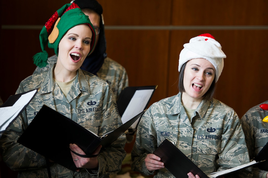 Two service members with holiday hats sing Christmas carols.