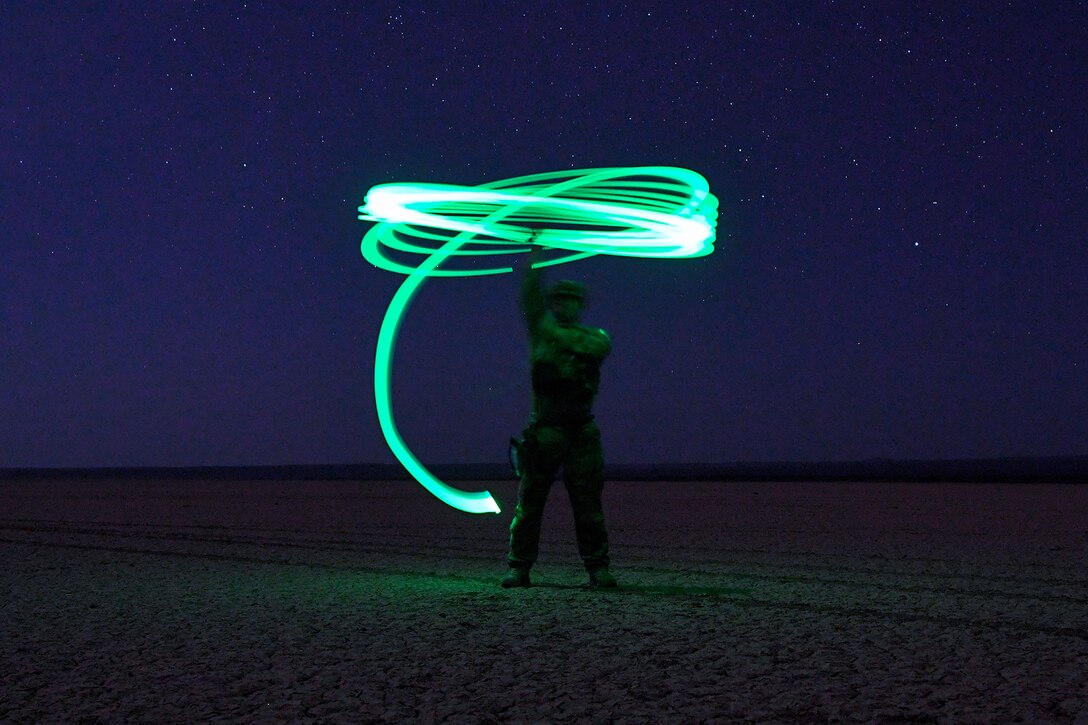 A service member swings a green light outside in the dark.