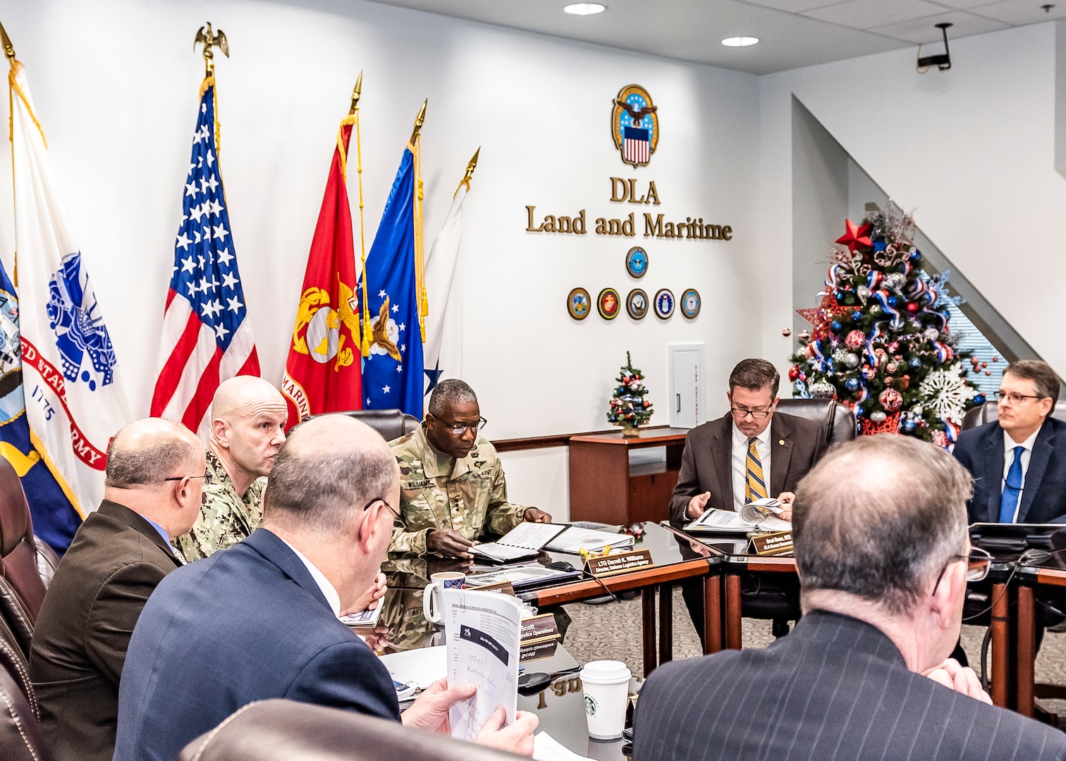 Senior leadership from DLA and Land and Maritime sit at a u-shaped table during a meeting