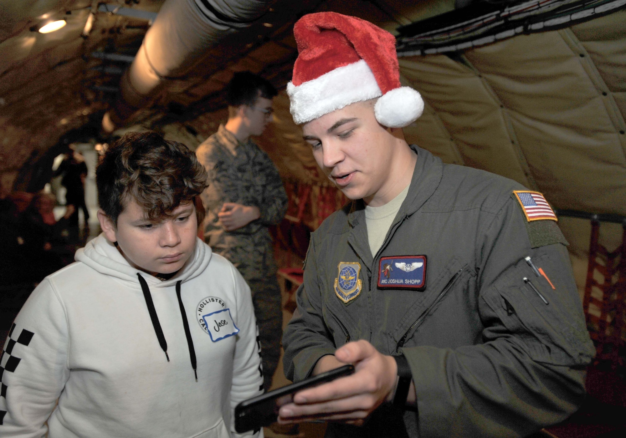 Airman 1st Class Joshua Shopp, 349th Air Refueling Squadron boom operator, shows footage from previous flights to Jose, a child from Big Brothers Big Sisters Dec. 19, 2018, at McConnell Air Force Base, Kansas. A static display of a KC-135 Stratotanker was available for viewing and aircrew members were on hand to answer questions and explain the mission of the aircraft. (U.S. Air Force photo by Staff Sgt. David Bernal Del Agua)