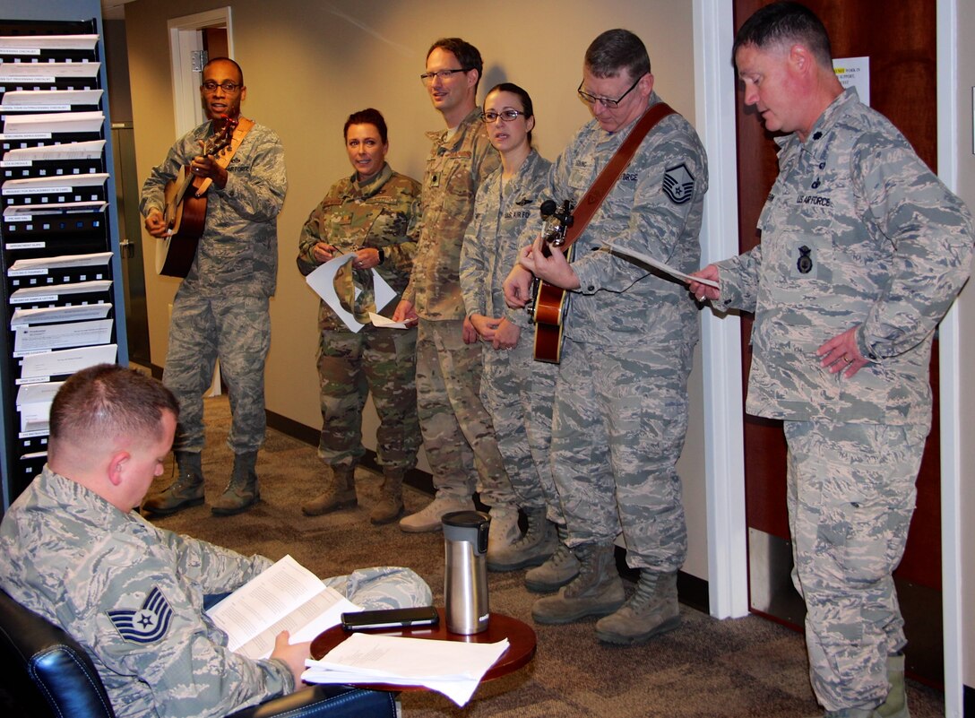 At left, Col. Lance Turner, the 932nd Mission Support Group's multi-talented commander, along with other officers and enlisted leadership, stopped by the 932nd Force Support Squadron customer service waiting area around lunch time in the headquarters building to share some holiday songs Dec 2, 2018, at Scott Air Force Base, Illinois. They sang various melodies during the Unit Training Assembly to help Airmen pass the time in the line. The other highly talented and experienced guitar player at second from right is Master Sgt. Tony Loving, who has been a vocalist and guitarist in a private community band for many years. All the action was captured for historical documentation by Master Sgt. Christopher Parr on his portable tripod and video phone camera system just outside the frame. (U.S. Air Force photo by Lt. Col. Stan Paregien)
