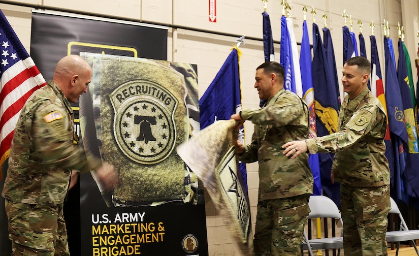 USAREC Commander, Maj. Gen. Frank M. Muth (left), USAMEB Commander, Col. Oscar H. Pintado (center) and USAMEB Command Sergeant Major, CSM Steven R. Laick, peel away a removable graphic of the Army shoulder insignia, revealing the USAREC Bell patch.  USAMEB and MSB Soldiers began wearing the USAREC patch Dec. 18