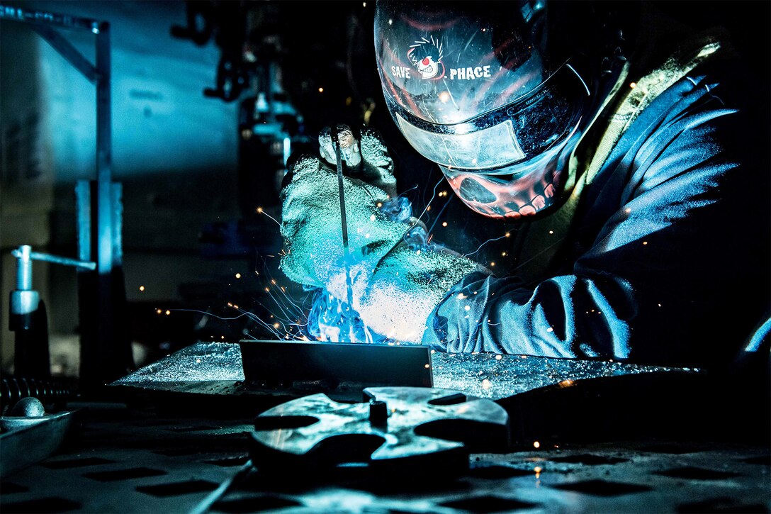 A service member welds in a workshop.