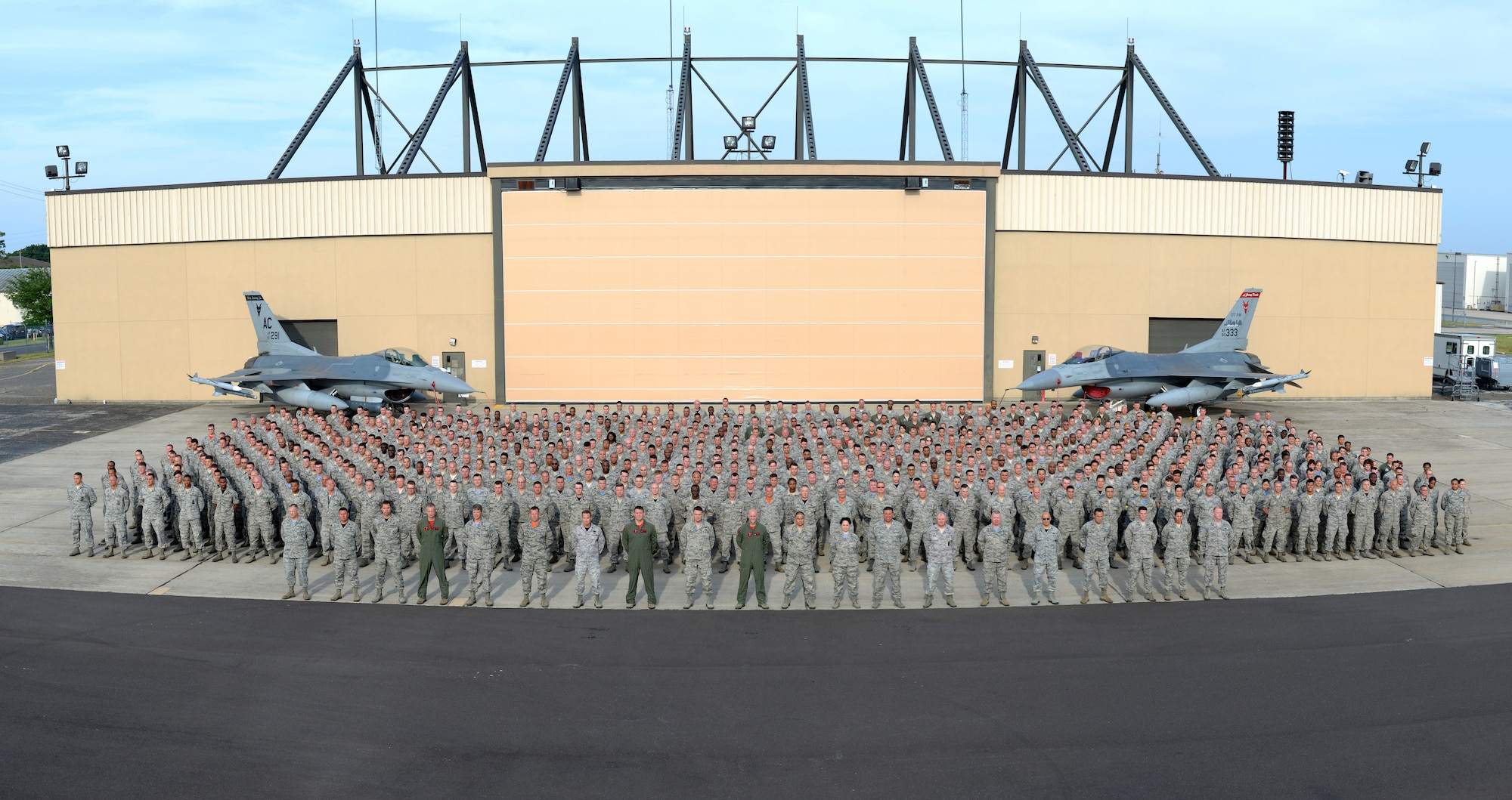A picture of members of the 177th Fighter Wing of the New Jersey Air National Guard posing for a group photo at the Atlantic City Air National Guard base in front of two U.S. Air Force F-16C Fighting Falcons and a hangar.