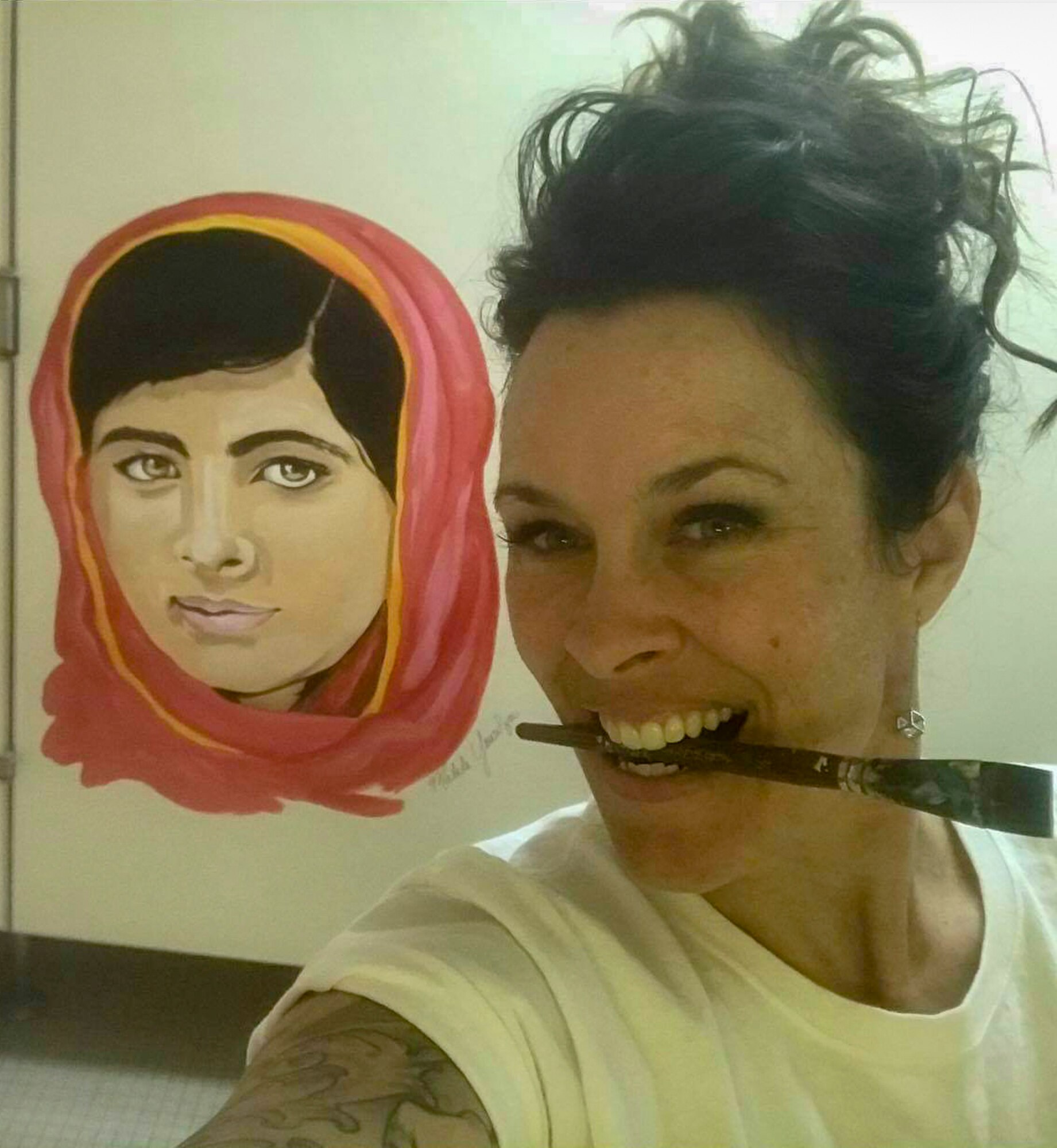 Sharon Smith, the wife of Maj. Brian Smith, a physical therapist with the 35th Medical Operations Squadron, takes a selfie next to her mural in Edgren High School at Misawa Air Base, Japan, in 2018. She creates a culture of positivity and affirmation through her art for the high school students. Smith painted a mural of Malala Yousafzi to inspire young women to stand up for what is right and encourage them to be brave. (Courtesy photo by Sharon Smith)
