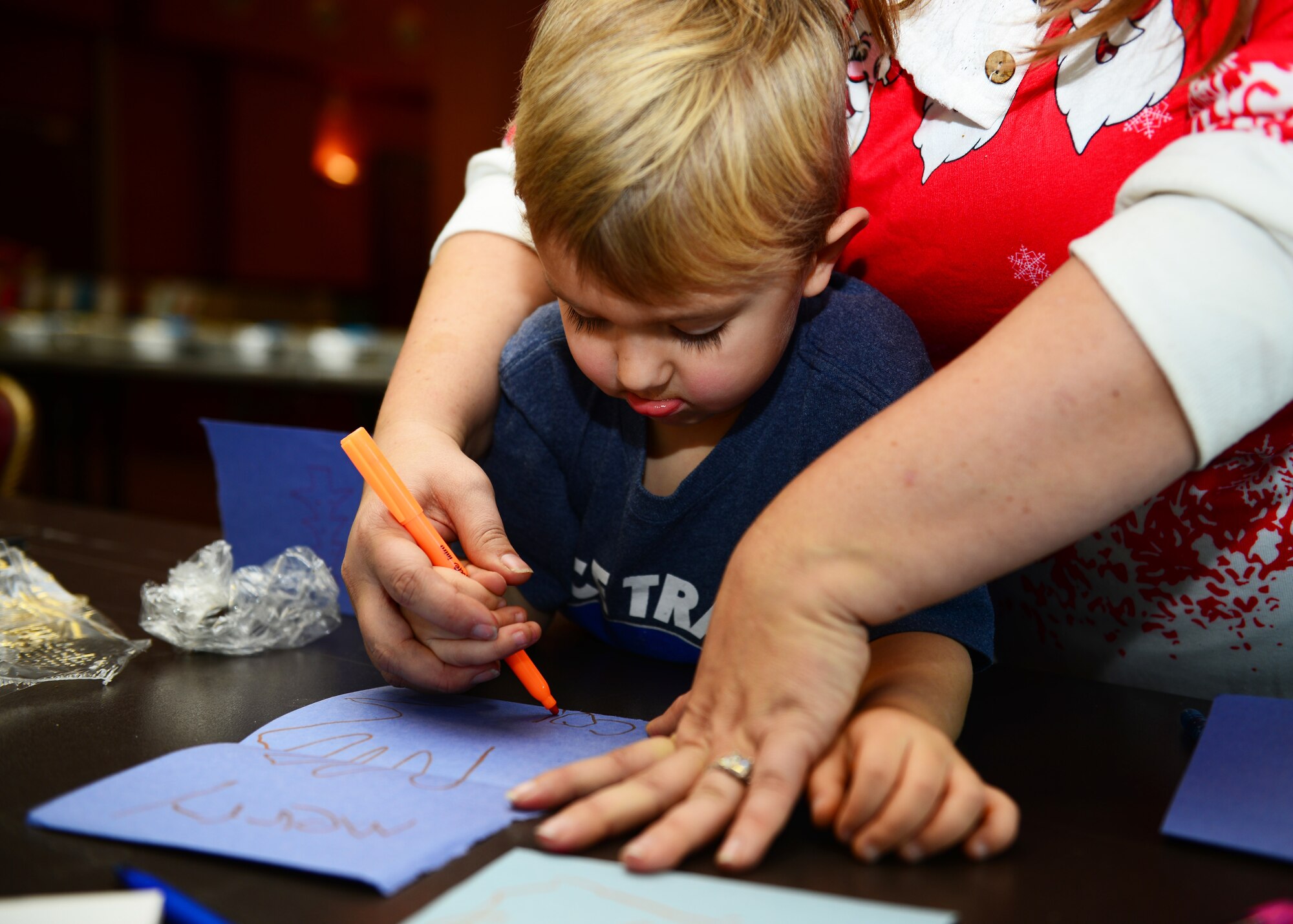 Connor Oden, 4, son of MSgt Michael Oden with the 606th Air Control Squadron, designs a Christmas card during a cookie drive at Aviano Air Base, Italy, Dec. 11, 2018. Connor was assisted by his mother, Rachel Oden, a member of Spouses of Aviano.