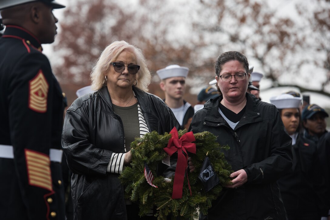 (Left) Sheryl Bice, Navy Wives Clubs of America national president, and (right) Amy Roberson, Navy Wives Clubs of America national vice president, walk a wreath dedicated to members of the Armed Forces that are or were prisoners of war or missing in action in honor of National Wreaths Across America Day at the Hampton National Cemetery in Hampton, Virginia, Dec. 15, 2018.