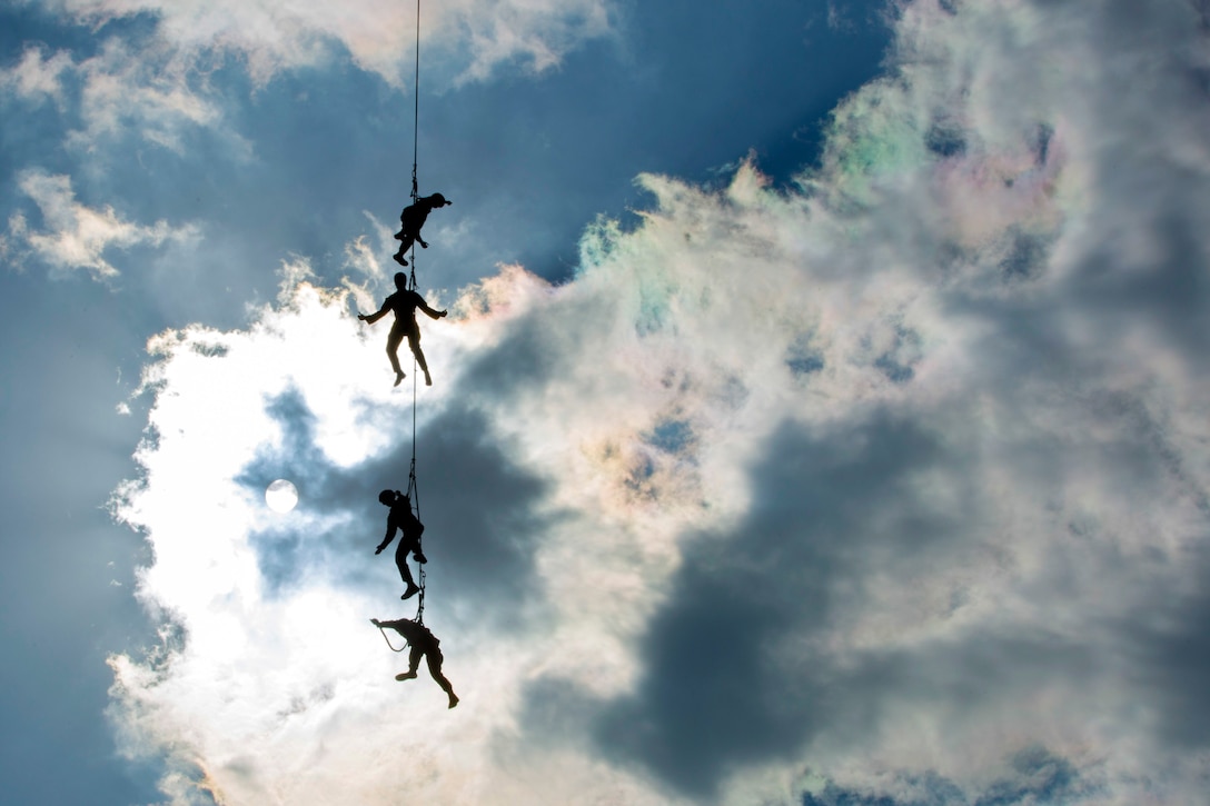 Marines hang from a rope from an off-screen helicopter.