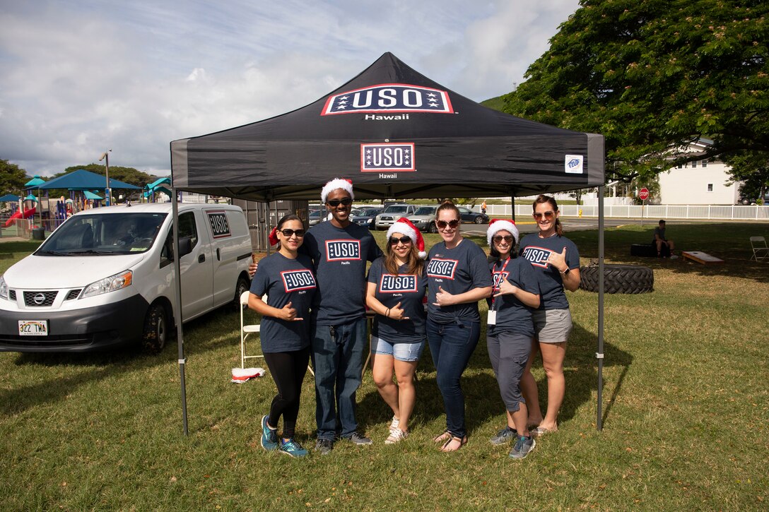Volunteers with the United Service Organizations (USO) pose in front of their tent during a Marine Corps Community Services (MCCS) event at Risely Field, Marine Corps Base Hawaii, Dec. 18, 2018. USO and MCCS provided food and drinks to single and unaccompanied U.S. Marines and Sailors on the installation. (U.S. Marine Corps photo by Sgt. Zachary Orr)