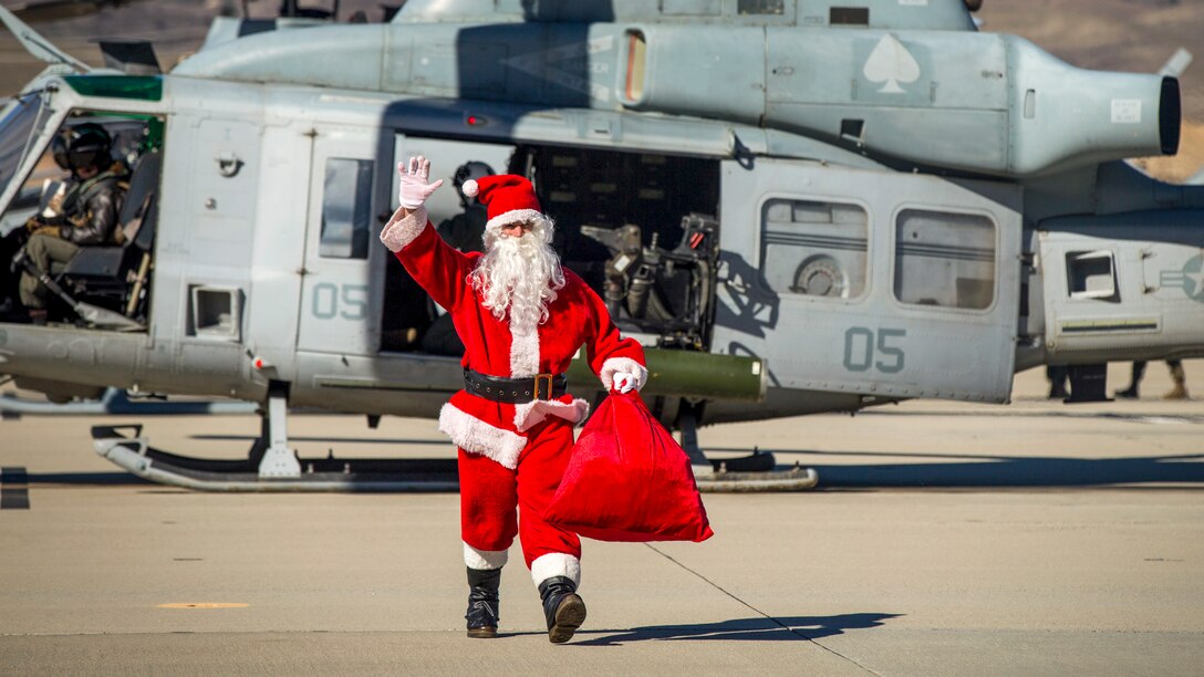 Santa Claus waves while walking away from a helicopter on a flightline.