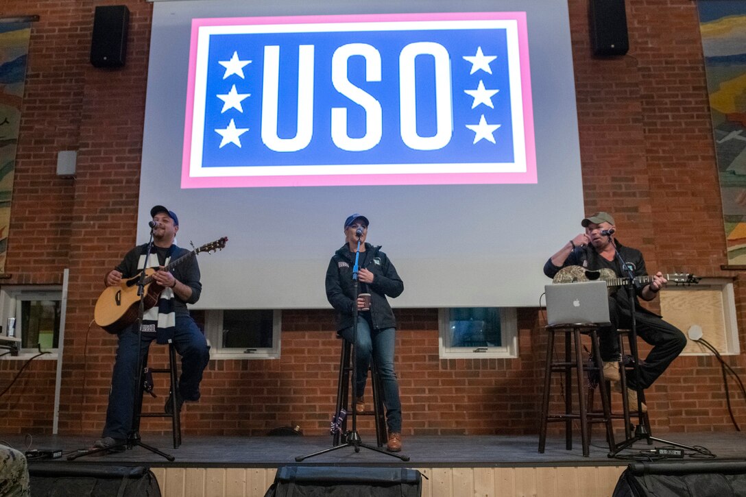Kellie Pickler performs on a stage with a USO logo in the background.