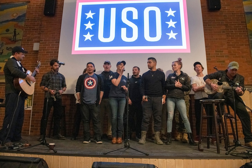 Performers sing on a stage with a USO logo in the background.