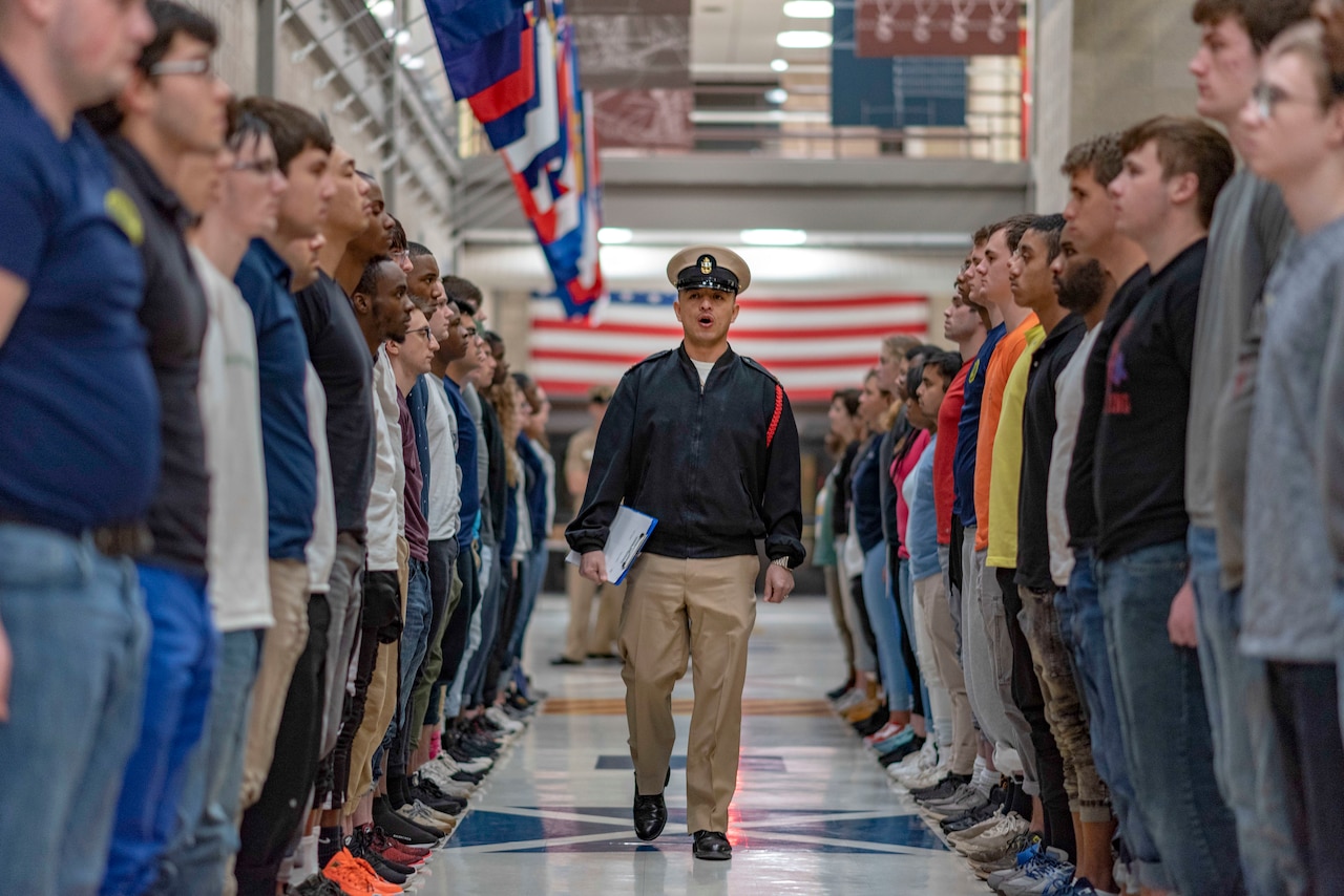 A sailor walks down the middle of two lanes of navy recruits facing each other.