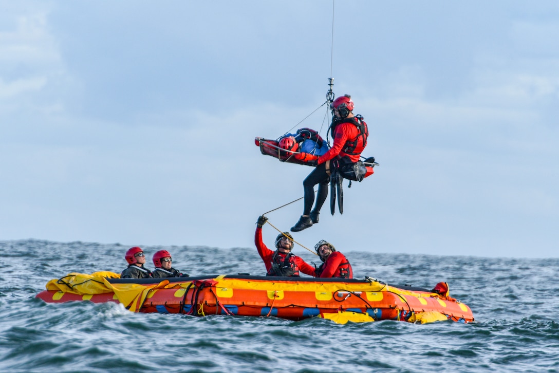 Airmen swim and hang from ropes over the ocean.