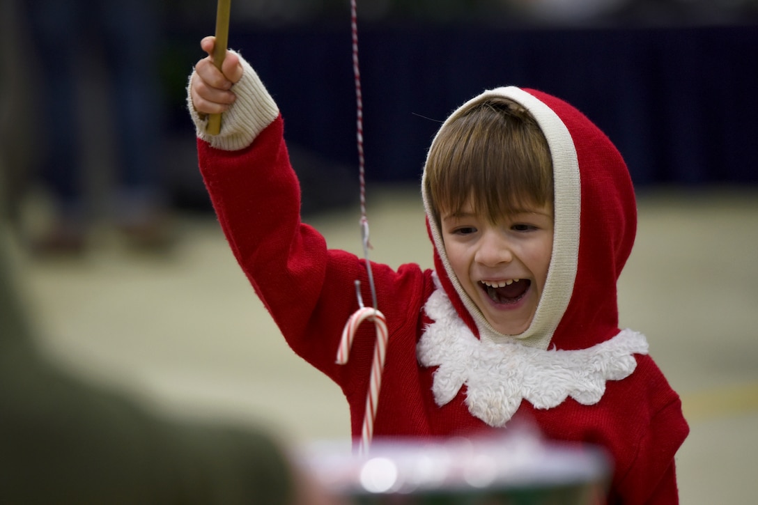 A child in a red Christmas outfit smiles while holding up a candy cane on a makeshift fishing pole.