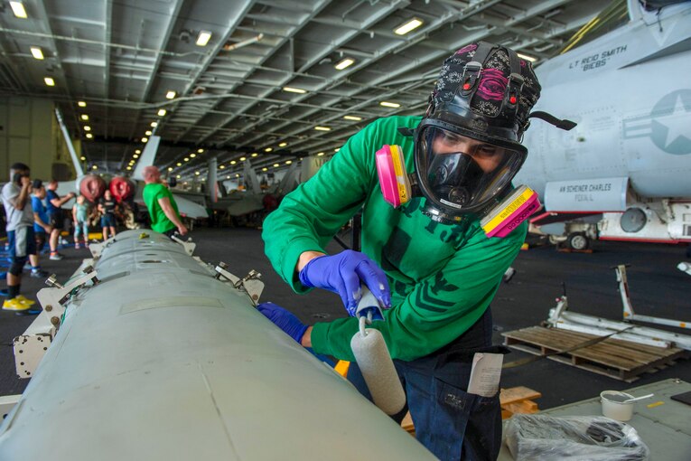 A sailor paints part of an airplane.