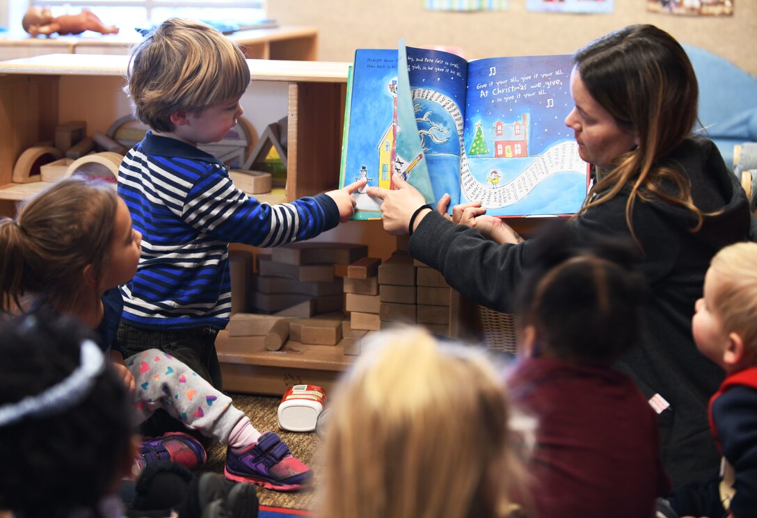 Fox Brookins, the son of Capt. Ryan K. Brookins, the 34th Bomb Squadron assistant director of operations, reads along as Crystal Emmons, a 28th Force Support Squadron program technician, reads "Pete the Cat Saves Christmas" at the McRaven Child Development Center on Ellsworth Air Force, S.D., Dec. 6, 2018. The book teaches children about giving to others during the Christmas season, while reading helps them to build language skills. (U.S. Air Force photo by Airman 1st Class Christina Bennett)