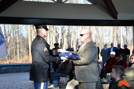 New York Army National Guard Sgt. Joshua Sanzo hands a folded American flag to a family member during a funeral service for Cpl. Lewis Smith, U.S. Army, during the burial mass at Gerald B.H. Solomon Saratoga National Cemetery, on Dec. 20, 2018. Smith served in the United States Army from 1958 to 1960.