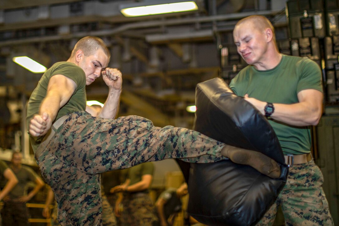 A Marine kicks a bag being held by another Marine.