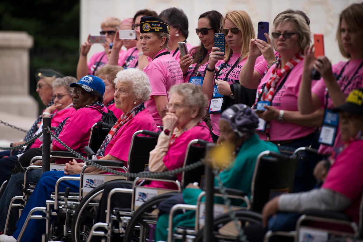A group of women standing and a group of women sitting in wheelchairs  watch a ceremony.