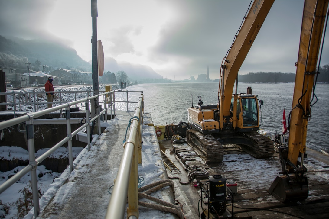 man on guidewall structure observes workers on barge in river