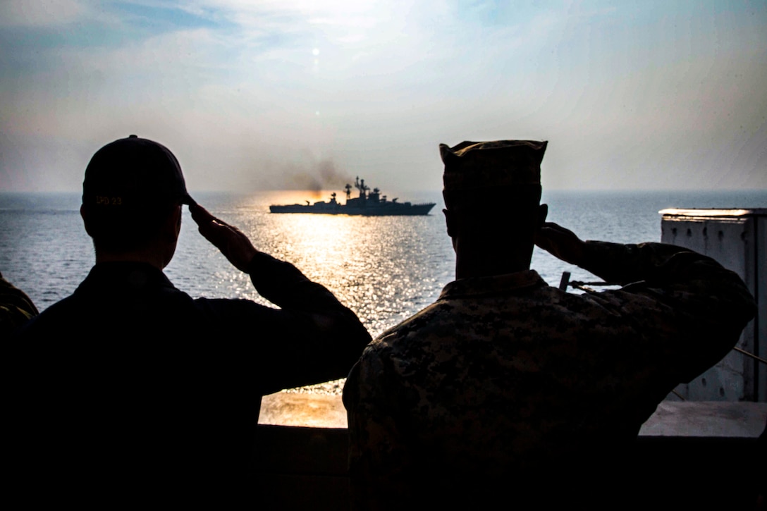 A Marine and a sailor salute an Indian naval vessel.