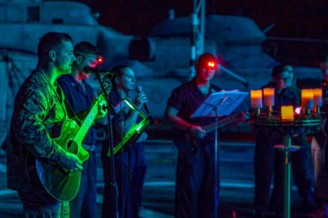 Marines and sailors sing and play instruments at night.