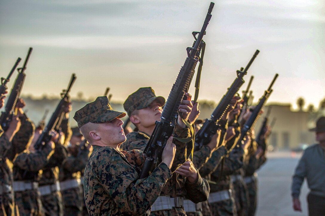 Marine Corps recruits inspect weapons while lined up.